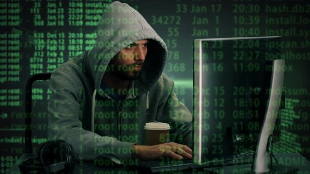 Mid Shot of a Hacker Wearing Hoodie Sitting at His Desktop Computer. Special Effects of Codes are Shown on the Screen. Shot on RED Cinema Camera 4K (UHD).