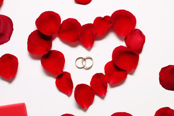 Gold wedding rings in heart from petals of a red rose on a white wooden table.