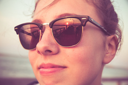 Vintage toned close-up face of a beautiful young teenage girl at beach with reflection of sunset in her sunglasses 