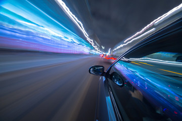 Obraz premium View from Side of Car moving in a night city, Blured road with lights with car on high speed. Concept rapid rhythm of a modern city.