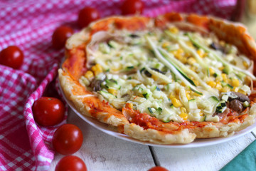 Homemade vegetarian pizza with lot of toppings: tomato sauce, mozzarella, zucchini, corn and champignons. Checkered napkin and cherry tomatoes laying around. Shallow depth of field. 