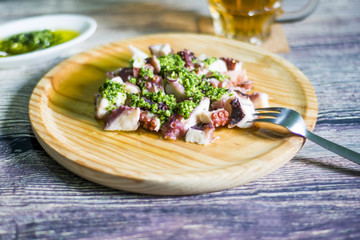 Octopus with paprika, a pitcher of beer and sauce on a wooden ta