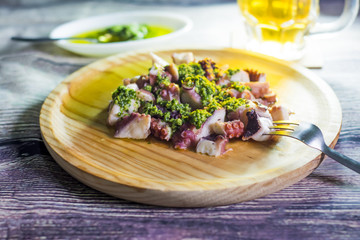 Octopus with paprika, a pitcher of beer and sauce on a wooden ta