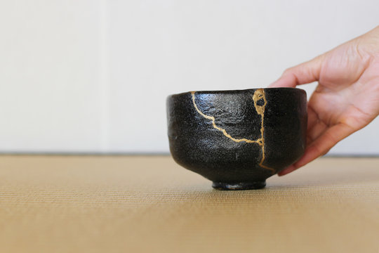 金継ぎされた黒楽抹茶茶碗を右手で置く畳の和室風景