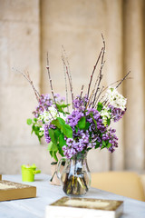 Branch with fresh blooming spring lilac flowers in vase, on table in the cafe