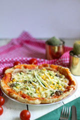 Homemade vegetarian pizza with lot of toppings: tomato sauce, mozzarella, zucchini, corn and champignons. Checkered napkin, cherry tomatoes and cacti laying around. Shallow depth of field.