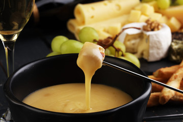 Gourmet Swiss fondue dinner on a winter evening with assorted cheeses on a board alongside a heated...