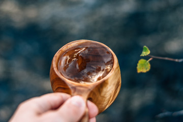 Hand holding a wooden cup filled with fresh mountain spring water