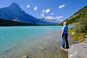 Woman looking at the beautiful view of clear turquoise lake and rocky mountains. Waterfowl lake. Canadian Rockies. Banff National Park. British Columbia. Canada.