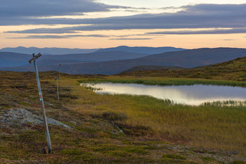 Hiking trail marking poles with lake and sunset