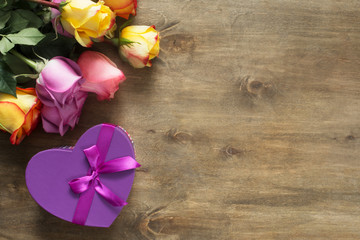 Purple and yellow roses, box present on wooden background