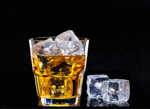 Glass of scotch whiskey and ice over black background.