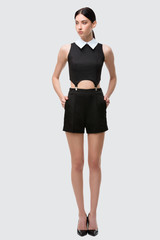 Fototapeta premium beautiful brunette girl in black shorts and top with a collar wearing heels over the gray background full-length isolated