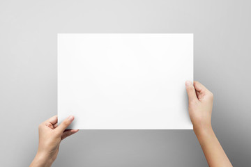 Woman hand holding blank paper sheet A4 size or letter paper on grey background.