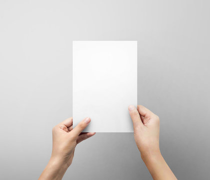 Woman hand holding blank paper sheet A5 size or letter paper on grey background.