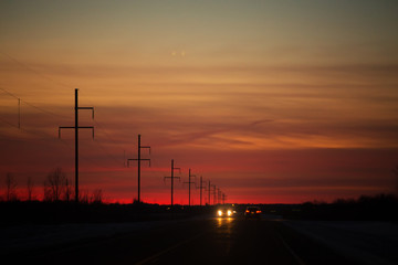 Fototapeta na wymiar Headlights and taillights of cars on a highway at night under a colorful sunset in rural landscape
