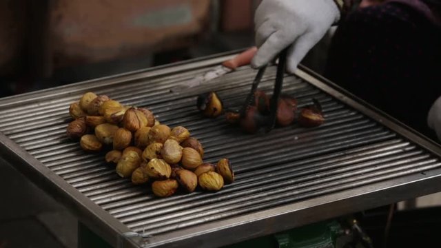 Man roasts chestnuts grilled on a city street.