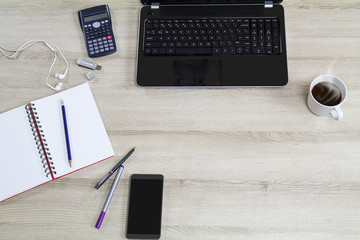 Computer laptop with mobile phone, office supplies and hot black coffee cup with steam on vintage wooden desk background view from above, business concept