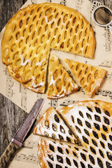 Homemade apple pie, plum pie on shabby wooden background and craft paper with a print of musical notes. Selective focus. Top view 