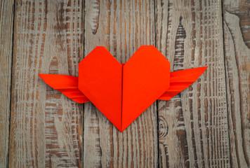 Red paper origami heart with wings on wood background .