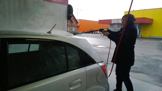 The man in the black coat washes the car at the point of self-hand car wash