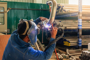 Industrial worker with protective mask welding metal piping using tig welder