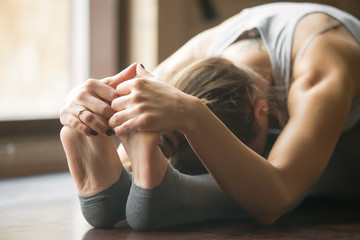 Close up of young woman practicing yoga, sitting in Seated forward bend exercise, paschimottanasana...