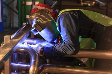 Industrial worker with protective mask welding metal piping using tig welder