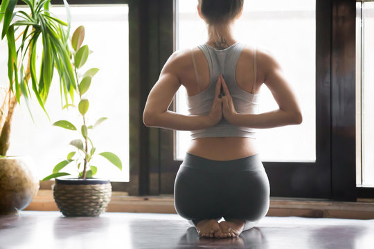 Young woman practicing yoga with namaste behind the back, sitting