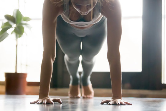 Young attractive woman practicing yoga, standing in Push ups, press ups, phalankasana exercise, Plank pose, working out, wearing sportswear, grey pants, bra, indoor, home interior background. Close up