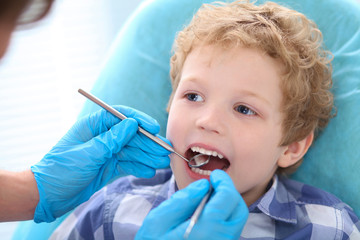 Close-up portrait of little boy opening his mouth wide during inspection of oral cavity by dentist.