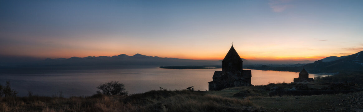 Panoramic view of the christian temple complex on the Sevan Lake at sunset, Armenia. Silhouettes of St. Jakob Church and Sevanavank. Armenian landmarks