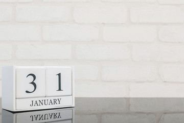 Closeup white wooden calendar with black 31 january word on black glass table and white brick wall...