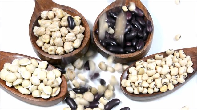 Red kidney bean, chickpeas, black eyd peas and white beans on a wooden spoon. Falling legumes on a white background.