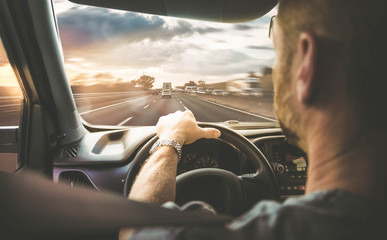Mann fährt mit Auto über eine befahrene Autobahn (Rückansicht) mit Gegenlicht