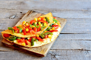 Stuffed vegetable omelet on wooden background with empty place for text. Fried omelet stuffed with red and green bell peppers and canned corn. Vegetarian eggs recipe. Rustic style. Closeup