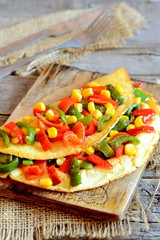 Delicious vegetable omelet on a wooden board. Fried omelet stuffed with red and green bell peppers and corn. Easy vegetarian breakfast omelet recipe. Vintage style. Closeup 