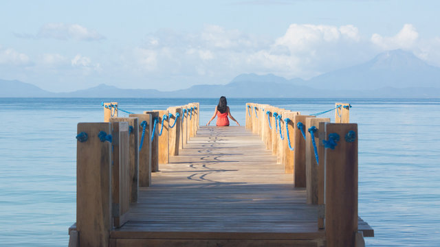 Perspective of Beautiful Traveler Woman in Red Dress, Sitting at End of Wooden Island Pier over the Sea - Palawan, Philippines