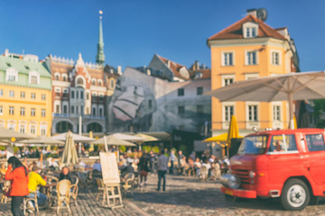 Red car and tourists in the summer cafe on Dome Square in the Old Town in a sunny summer day. Blurry