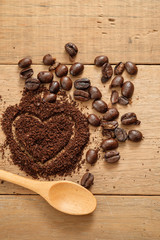 ground coffee in heart shape close to coffee beans on wooden table