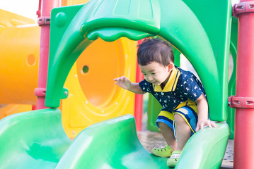 Fototapeta na wymiar Little Asian kid playing slide at the playground under the sunli