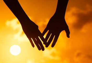 Man and woman's hand coming together against beautiful sunset. 