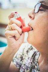 Close-up of senior woman in glasses breathing inhaler