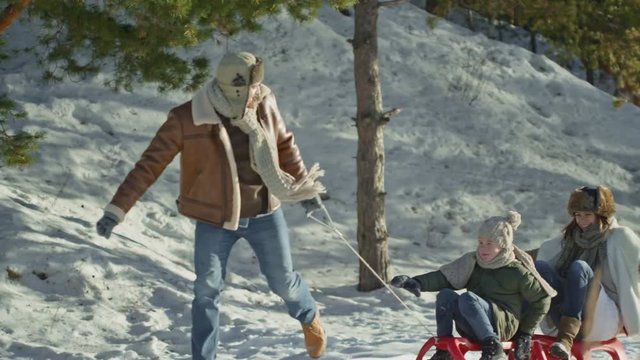 Tracking of happy woman and boy sitting on sled and being pulled by laughing man 