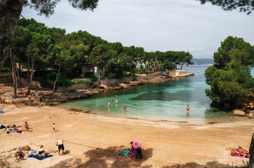 Little Pellicer Beach in Santa Ponsa with green azure water, bathers and vacationers in a sunny...