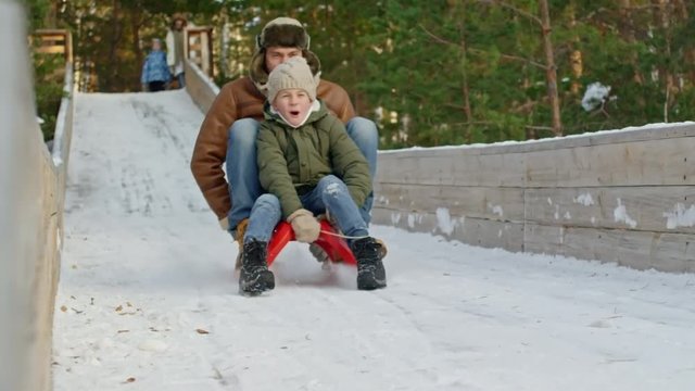 Slow motion joyous little boy and his father sledding on slide in winter 