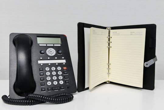 Black IP Phone and opened notebook on the white table