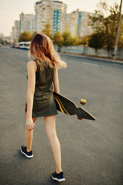 Beautiful young tattooed woman with his longboard on the road in the city in sunny weather