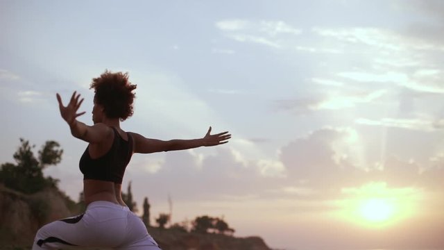 African American girl doing yoga asana standing on rocks by the sea in slowmotion. Silhouette