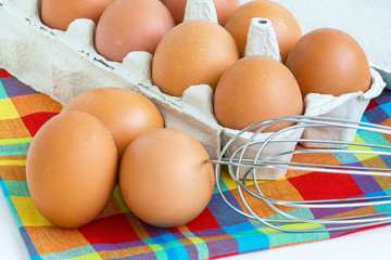 Oeufs dans leur boîte et batteur manuel sur fond de tissu madras